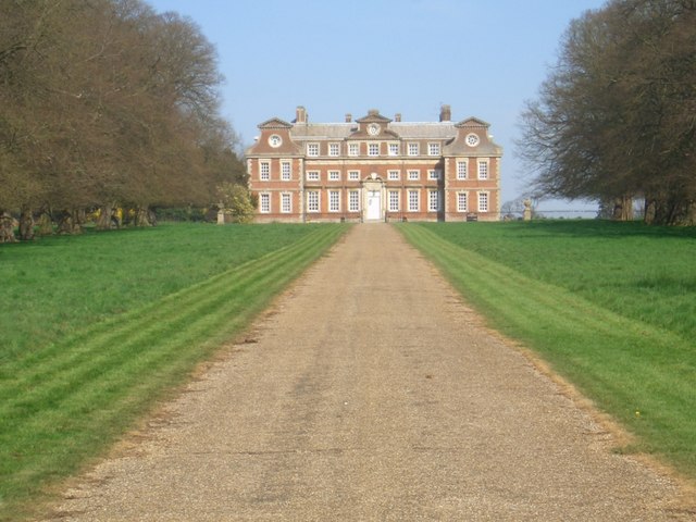 Raynham Hall viewed along the avenue. The documented building anchors a legend often encountered first through one famous staircase photograph.